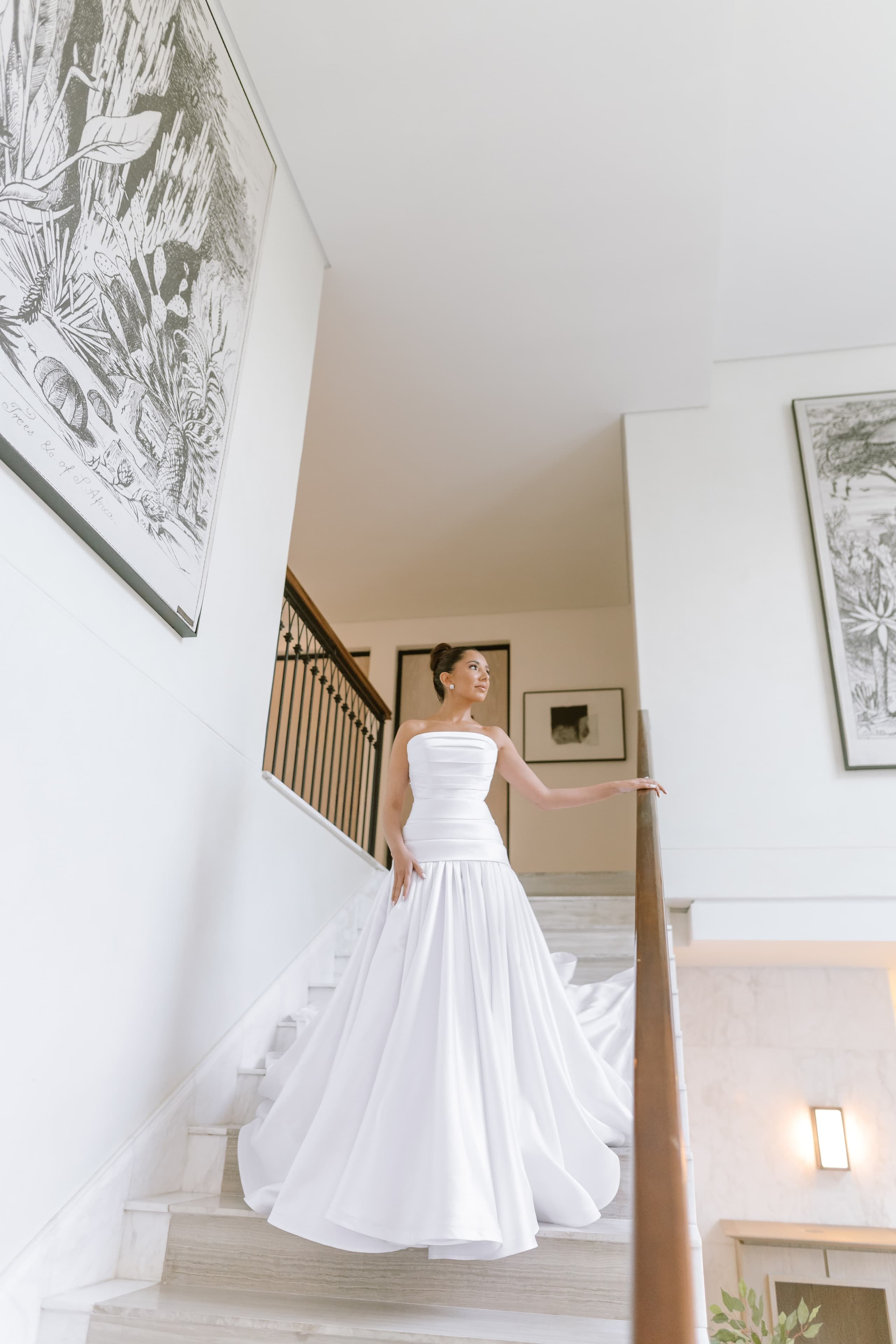 A bride in a strapless white gown stands elegantly on a modern marble staircase