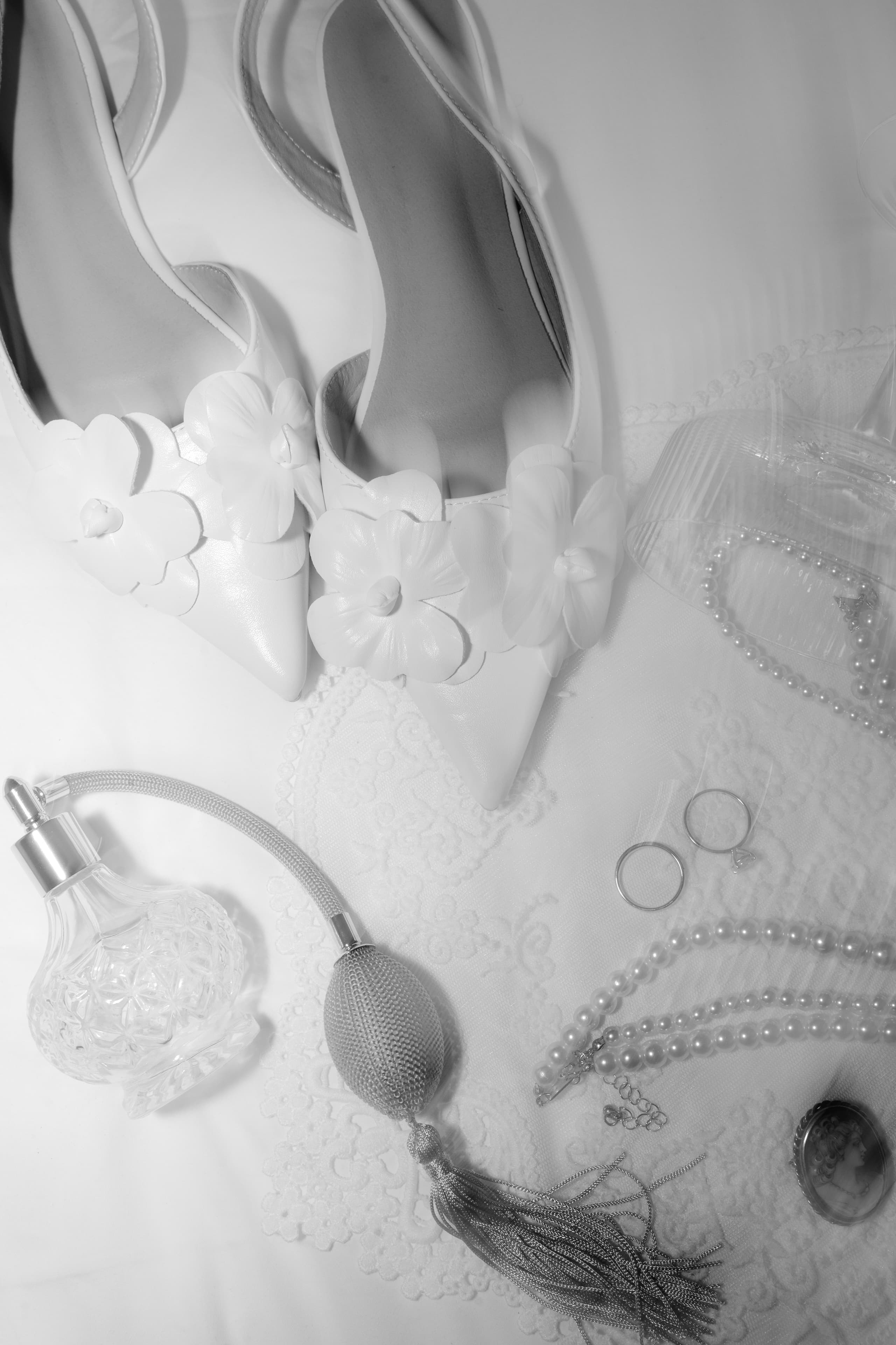 Elegant white wedding shoes arranged with vintage perfume bottles, rings, and pearl necklaces on lace