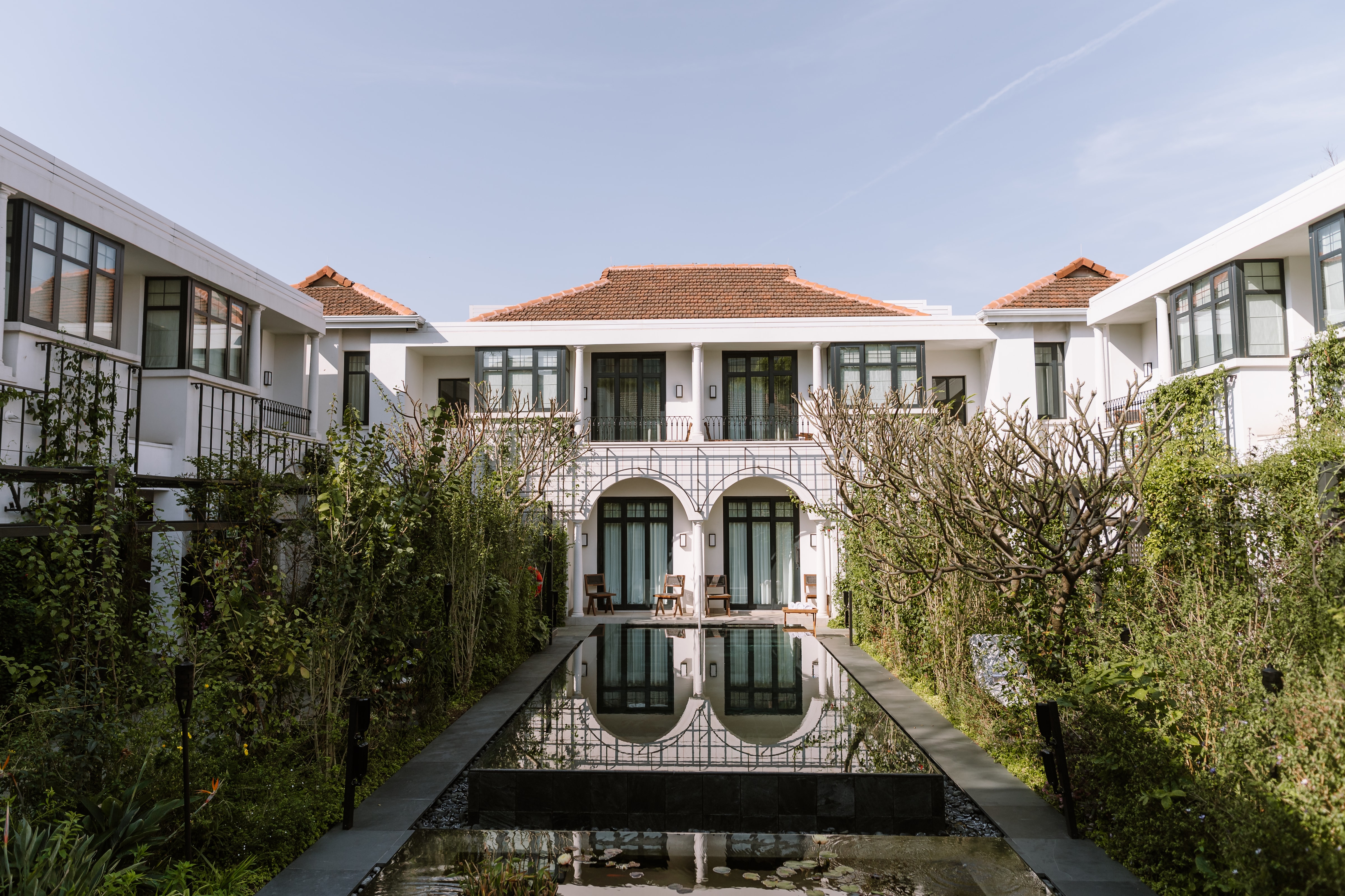 A serene courtyard featuring a long reflective pool surrounded by lush greenery and white architecture